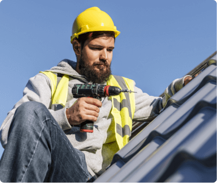 a man wearing a hard hat and a yellow vest holding a drill, working on roof